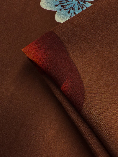 Close-up of Super Cheap Fabrics' Designer Rayon - Orchard Pop (145cm), showing smooth brown fabric with a folded corner, red curved pattern, and partial light blue floral design—ideal for vibrant prints.