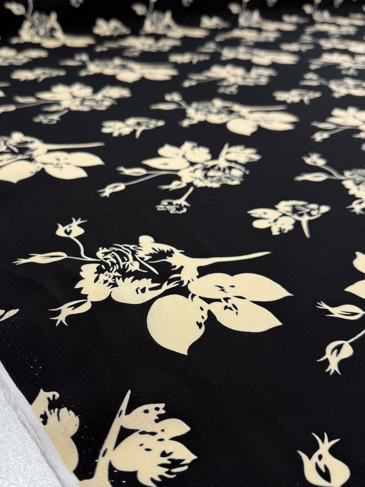 A close-up of Super Cheap Fabrics' Designer Rayon - Moonflower Silhouette (147cm), showing black fabric with a cream floral and leaf pattern, displayed flat.
