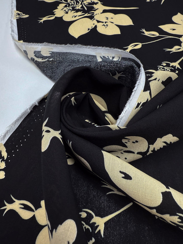 Designer Rayon - Moonflower Silhouette by Super Cheap Fabrics, 147cm wide, features a black base with beige floral print, displayed partially unrolled to show front and back; unfinished edges highlight texture and selvage.