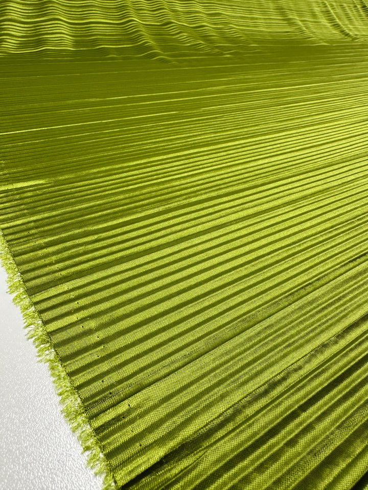 A close-up of the vibrant Chartreuse Metallix Pleat fabric from Super Cheap Fabrics, featuring fringed edges and spread out across a flat surface. The lightweight polyester material forms a textured, wavy pattern that highlights its sheen and softness.