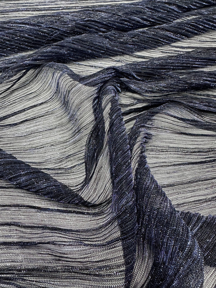 A detailed view of the Metallix Pleat - Cobalt Metal by Super Cheap Fabrics, showcasing its shimmering polyester material with intricate, wavy pleats in metallic silver and deep navy hues, giving it a textured and luxurious look.