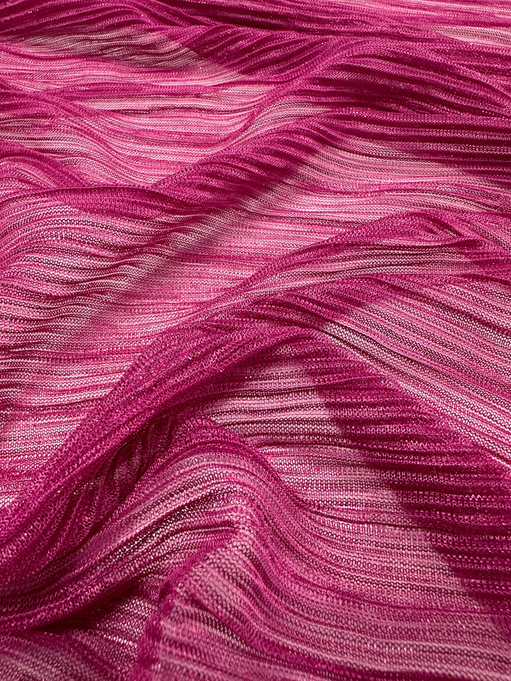 A close-up of the Metallix Pleat fabric in Hot Pink from Super Cheap Fabrics showcases its pleated polyester design, featuring varied shades and textures. This lightweight 140cm fabric flows gracefully, forming dynamic patterns with light and shadow that emphasize its delicate and intricate structure.