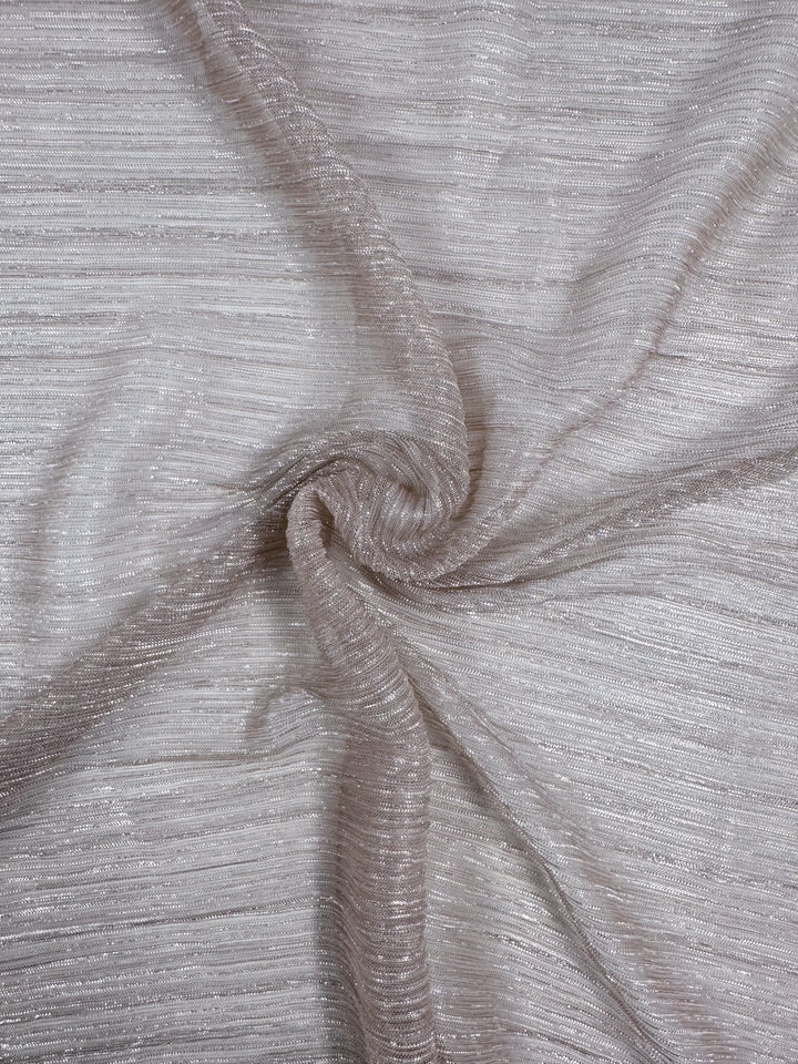 The Metallix Pleat - Blush - 140cm from Super Cheap Fabrics showcases a close-up of textured, shimmering polyester fabric in light beige with a blush tint, artfully gathered into a spiral pattern at the center. This lightweight fabric is designed with fine horizontal lines that reflect light and create a subtle glistening effect.