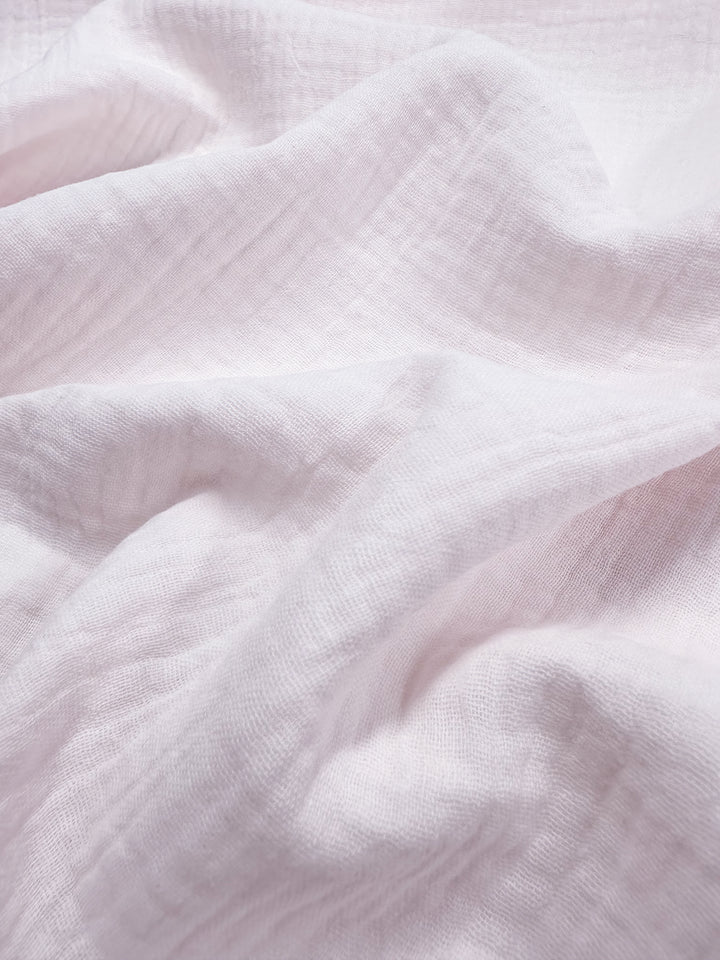 Close-up image of the soft, slightly pink fabric from Super Cheap Fabrics, showcasing gentle folds and a slightly textured surface. The 135cm wide muslin is arranged to create subtle shadows and highlights that emphasize its light, airy quality.