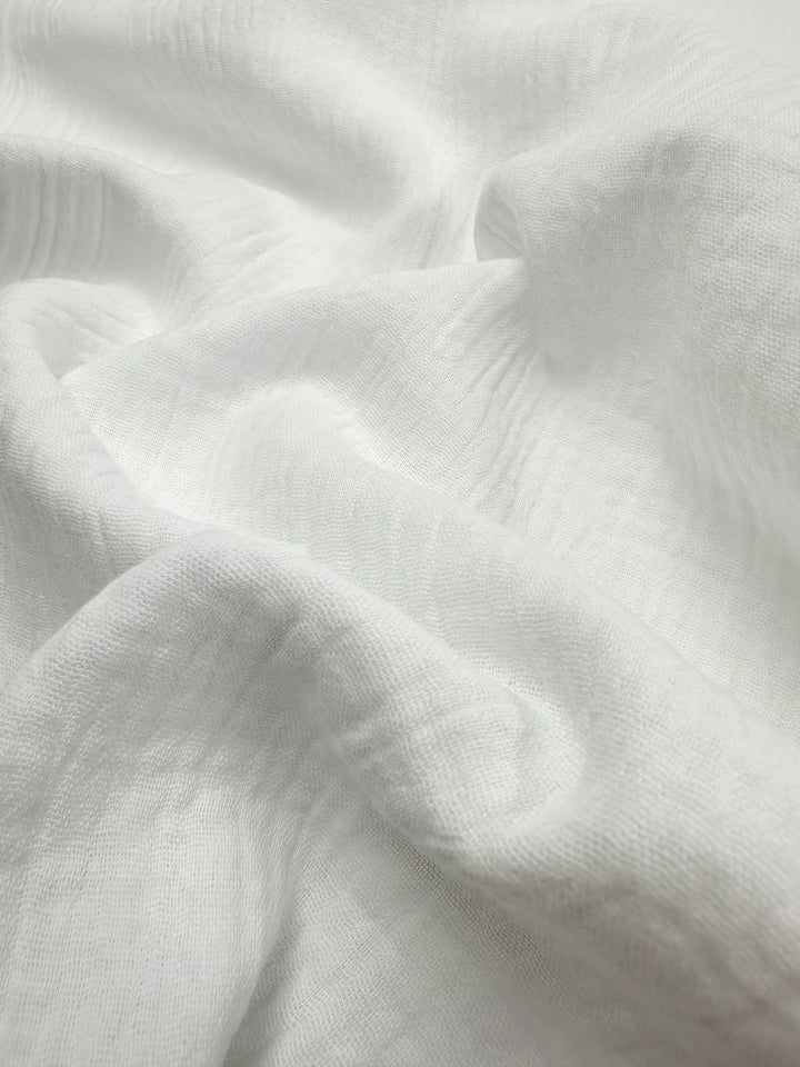 A close-up of the "Muslin - Snow White - 135cm" by Super Cheap Fabrics highlights its soft, wrinkled texture. The surface is smooth and slightly sheer, with gentle folds and natural shadows that enhance the delicate look of this reusable material.