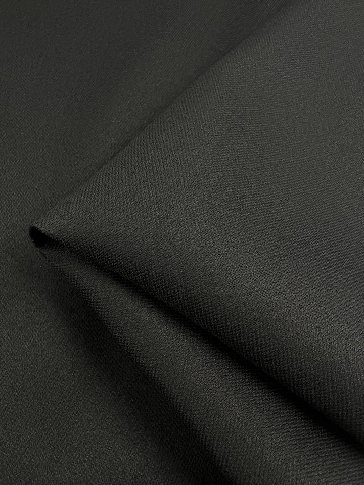 Close-up view of a piece of the Stretch Cotton Twill - Black Night fabric from Super Cheap Fabrics, displaying its dark green, medium weight texture. The material appears to be smooth and slightly reflective, with fine, even weaves that create a subtle, elegant pattern reminiscent of high-quality cotton twill.