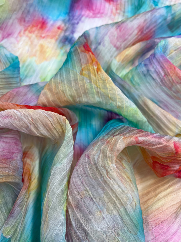 A close-up of Super Cheap Fabrics' Textured Tencel - Candy Clouds - 136cm, showcasing a vibrant tie-dye pattern. The intermingling shades of blue, pink, orange, yellow, and green create a soft, flowing texture that underscores the fabric’s sustainability.