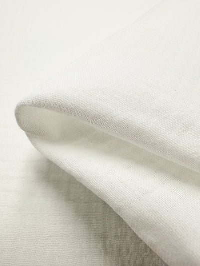 The image features a close-up of the Super Cheap Fabrics' Muslin - Ivory - 135cm, highlighting its softly textured organic surface and delicate weave. The lightweight and airy nature of this muslin fabric makes it an ideal choice for clothing or bedding.