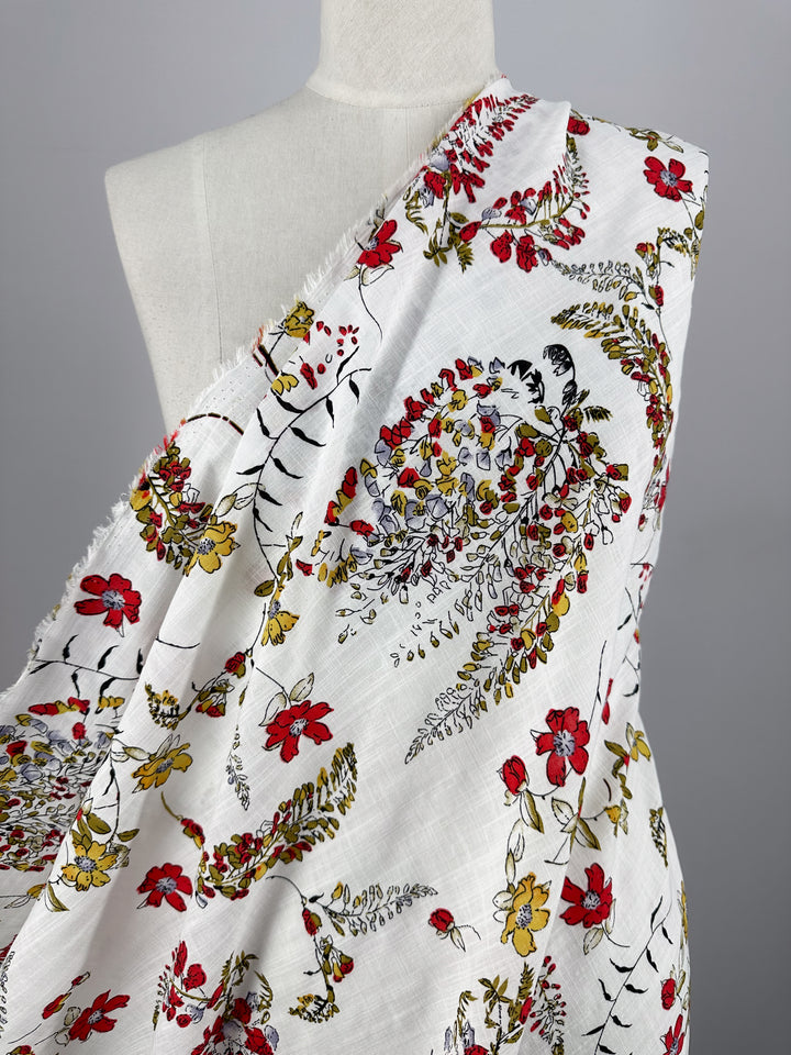 The Linen Blend - Scarlet Vine by Super Cheap Fabrics is draped over a mannequin, displaying vibrant red, yellow, and green floral patterns on white. Perfect for summer outfits, this breathable fabric combines lightweight comfort with effortless style. Width: 145cm.