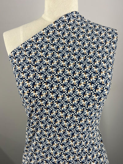 Set against a plain grey background, a mannequin displays an elegant asymmetrical garment featuring a blue and white floral pattern. This stylish piece, crafted from the medium-weight Textured Lycra - Mosaic - 150cm by Super Cheap Fabrics, drapes gracefully over one shoulder for a modern and chic look.