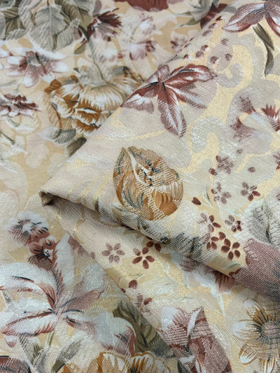 Close-up of a folded Designer Brocade - Vintage fabric from Super Cheap Fabrics, showcasing an intricate floral pattern in cream, beige, and brown tones. This medium-weight fabric features leaves and flowers that create an elegant tapestry-like appearance, reminiscent of Italian craftsmanship.