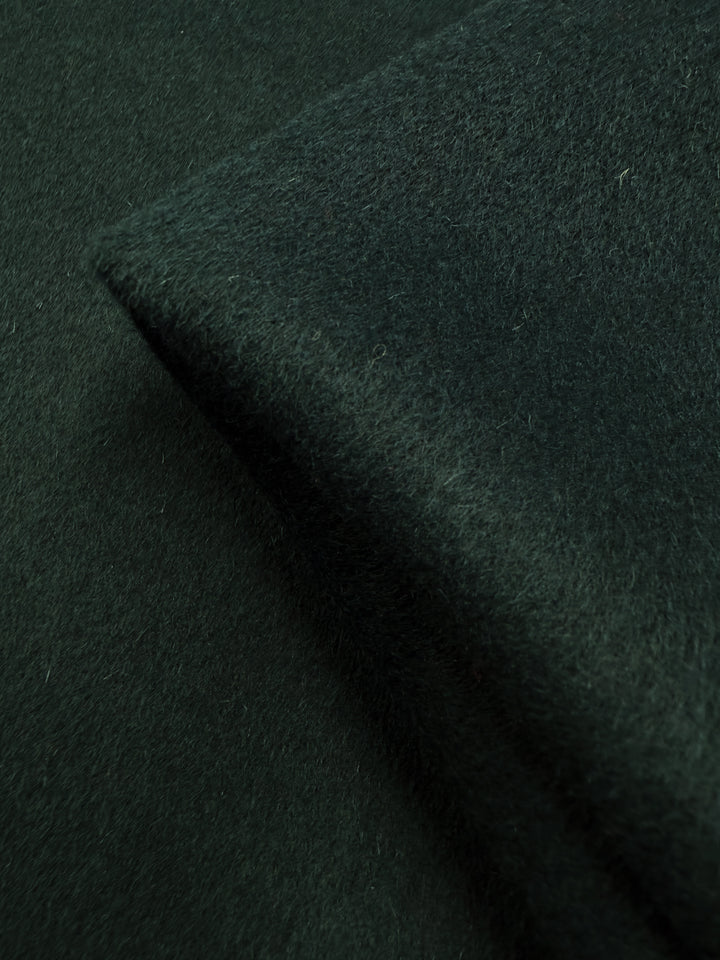 A close-up of Super Cheap Fabrics' Wool Cashmere in Sea Moss (146cm) highlights its luxurious, soft, fuzzy dark green texture and a neatly folded edge on a flat surface.