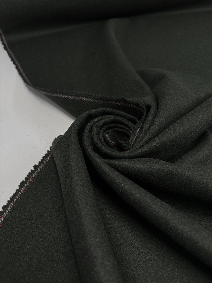 A close-up of Super Cheap Fabrics’ Melton Wool - Rosin Marle - 150cm, neatly folded into a swirl, highlights its smooth texture and subtle frayed edge—ideal as a heavyweight wool fabric for outerwear.