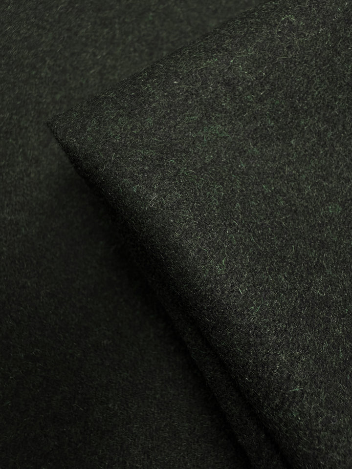 A close-up of two overlapping pieces of Super Cheap Fabrics’ Melton Wool - Rosin Marle (150cm), showcasing the soft, slightly fuzzy texture and rich dark green color typical of this heavyweight wool fabric.