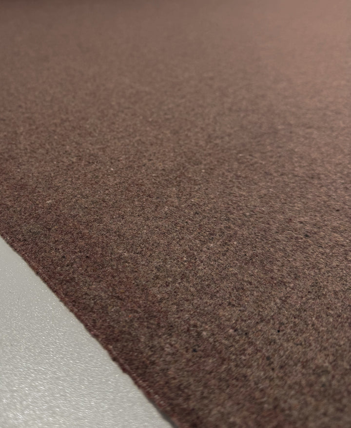 A close-up of Super Cheap Fabrics' Melton Wool - Cognac - 150cm shows its rich texture against a smooth, light gray surface, highlighting the contrast between the heavy wool and sleek background.