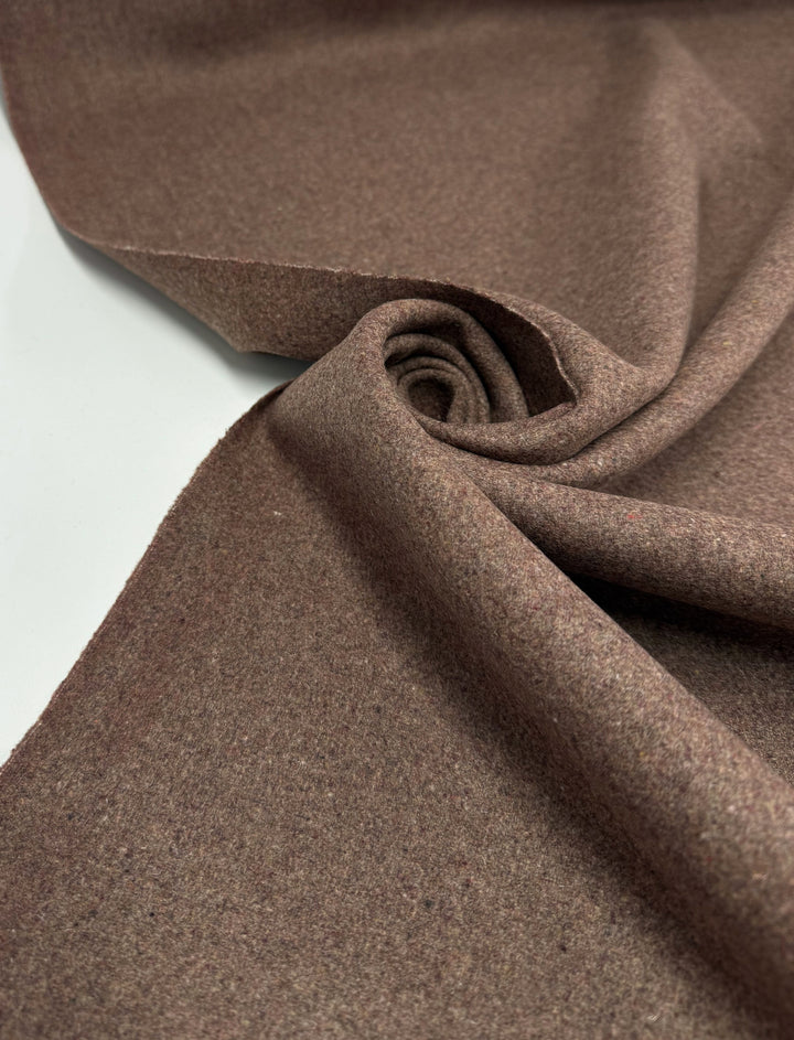 A close-up of Super Cheap Fabrics' Melton Wool - Cognac - 150cm, partially rolled on a white surface, highlights the classic outerwear fabric’s soft texture and thick, heavy quality.