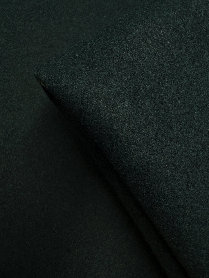 A close-up of Super Cheap Fabrics' Melton Wool - New Scarab - 154cm reveals its soft, textured dark green surface. Lighting highlights the fabric’s thickness and color depth, making it ideal for durable outerwear.