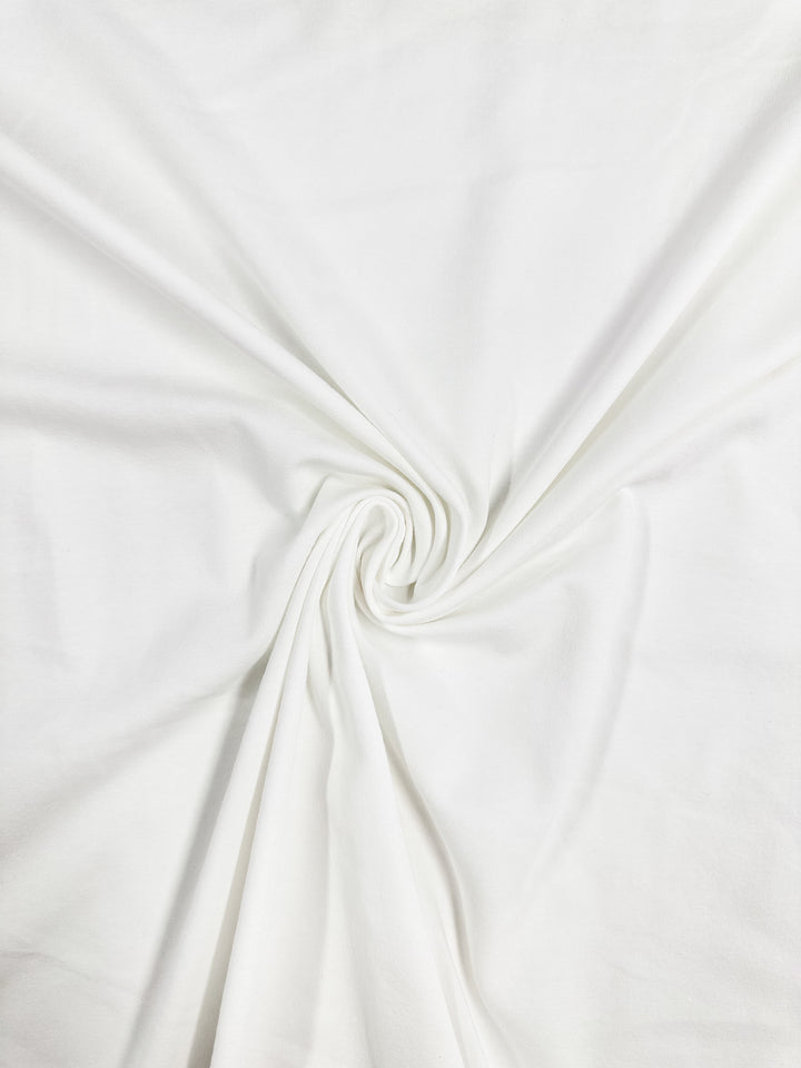 A close-up of Super Cheap Fabrics' Cotton Lycra in White, 140cm, reveals a central swirling pattern forming a spiral. The medium-weight fabric looks soft and smooth.