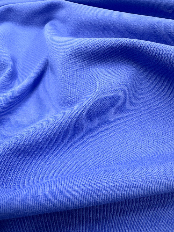 Close-up of vibrant Super Cheap Fabrics' Cotton Lycra in Nebulas Blue, 165cm wide. The fabric features a smooth, slightly ribbed texture and medium weight cotton that gathers in soft folds, highlighting its flexibility and softness.