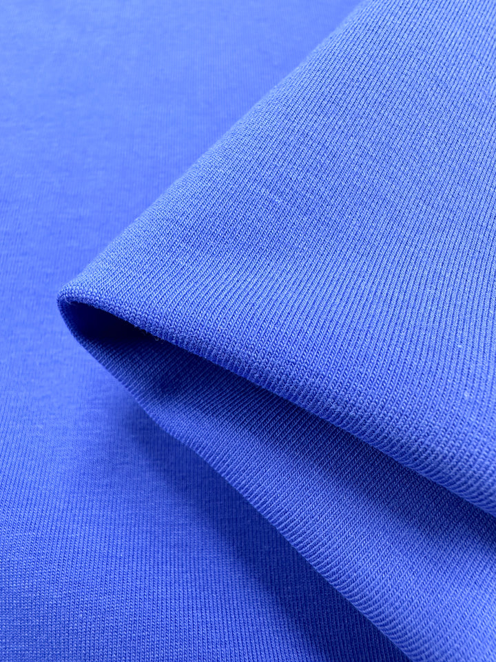 Close-up of folded Super Cheap Fabrics' Nebulas Blue Cotton Lycra, 165cm wide. The ribbed texture is enhanced by the lighting, highlighting its smooth surface and fine knit pattern that exudes softness and flexibility in this medium-weight fabric.