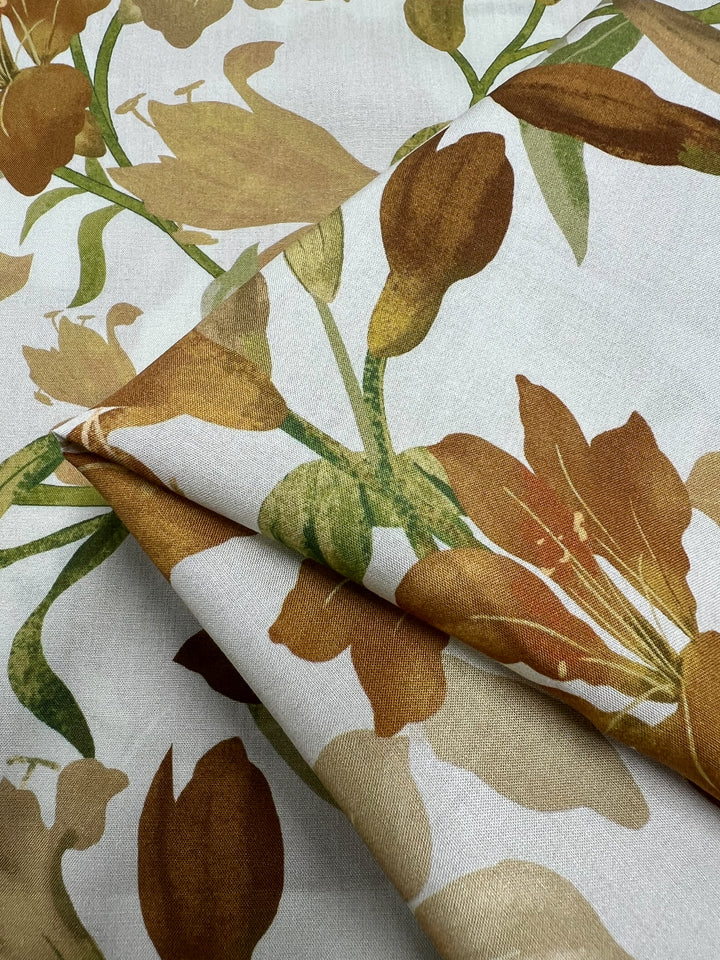 A close-up of the Designer Rayon - Autumn Gold - 145cm by Super Cheap Fabrics showcasing its versatile design with a printed floral pattern in shades of brown and green on a white background. The neatly folded fabric reveals the detailed design of flowers and leaves.