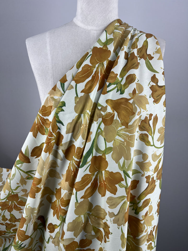 Draped on a mannequin, the Designer Rayon in Autumn Gold by Super Cheap Fabrics features vibrant floral prints in shades of yellow and green. Set against a plain gray background, this versatile fabric measures 145cm and beautifully highlights its intricate design, making it suitable for any setting.