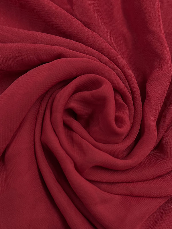 A close-up of the Hi-Multi Chiffon in Savvy Red from Super Cheap Fabrics showcases its sheer and lightweight fabric elegantly swirled into a spiral pattern, creating a textured and layered appearance. The soft and smooth texture of this 150cm wide material highlights the richness of its vibrant red hue through its swirling folds.