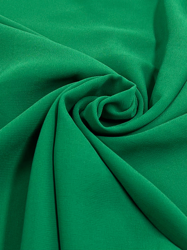 A close-up of the Hi-Multi Chiffon - First Tee fabric from Super Cheap Fabrics, featuring a spiral pattern in green. The lightweight material has a smooth and soft feel with a subtle texture. The dynamic folds create a swirling design at the center, reminiscent of floaty tops.