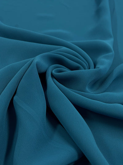 A close-up view of the Hi-Multi Chiffon in Turkish Tile, a product by Super Cheap Fabrics, featuring a smooth, silky texture draped in swirling folds. This lightweight fabric is reminiscent of those used for airy tops and showcases a soft, rich appearance with subtle highlights that create elegant curves and depth.