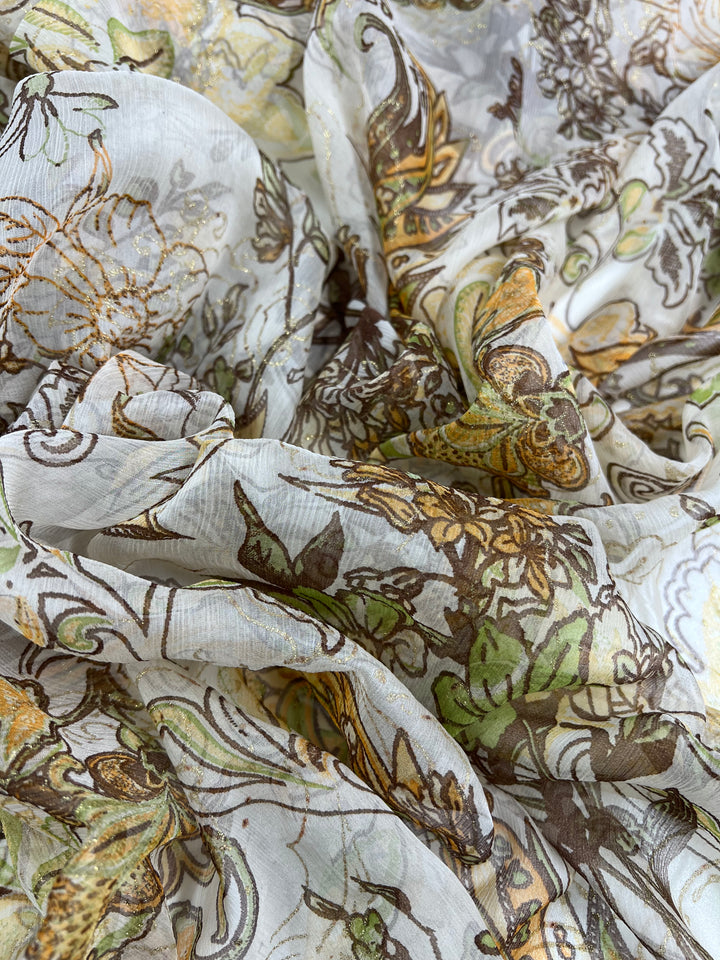 A close-up image of intricately patterned Pure Printed Silk - Jaipur - 130cm by Super Cheap Fabrics, featuring yellow, green, and brown floral motifs. The lightweight material is lightly crumpled, showcasing the detailed design and texture against a light, translucent fabric background.