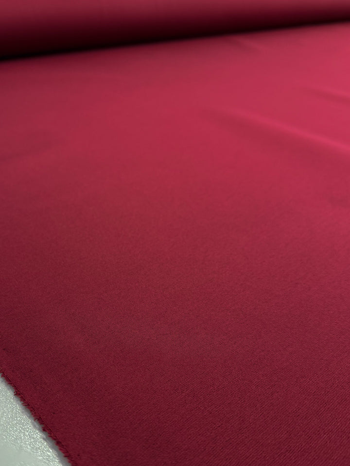 A close-up shows Milano Ponte - Cabernet by Super Cheap Fabrics, a smooth, heavy-weight, deep red 160cm ponte fabric with a soft, even texture—ideal for creating structured garments.