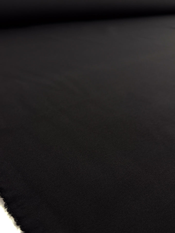 A close-up of Super Cheap Fabrics' Milano Ponte - Black - 160cm shows its large, smooth, heavyweight surface with subtle texture and the fabric’s edge on the left.