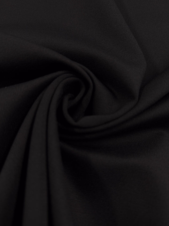 Close-up of Super Cheap Fabrics’ Milano Ponte - Black (160cm), showing smooth fabric with a swirling, twisted center that creates soft folds and subtle shadows.