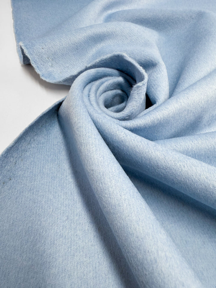 A close-up of Super Cheap Fabrics' Wool Cashmere - Cool Blue (152cm) shows the fabric gently spiraled, highlighting its luxurious softness, smooth texture, and delicate folds.