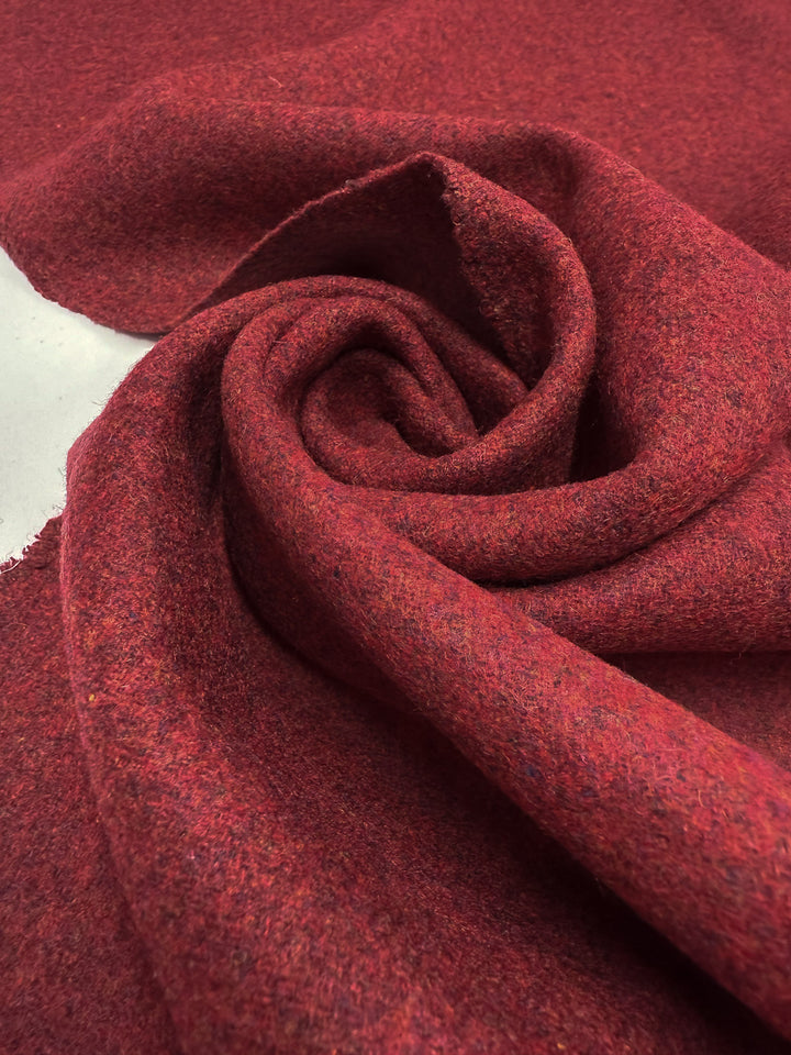 A close-up of Super Cheap Fabrics' Wool Cashmere in Syrah Marle (152cm) shows luxurious red fabric with visible fibers, soft folds, and a textured spiral arrangement.