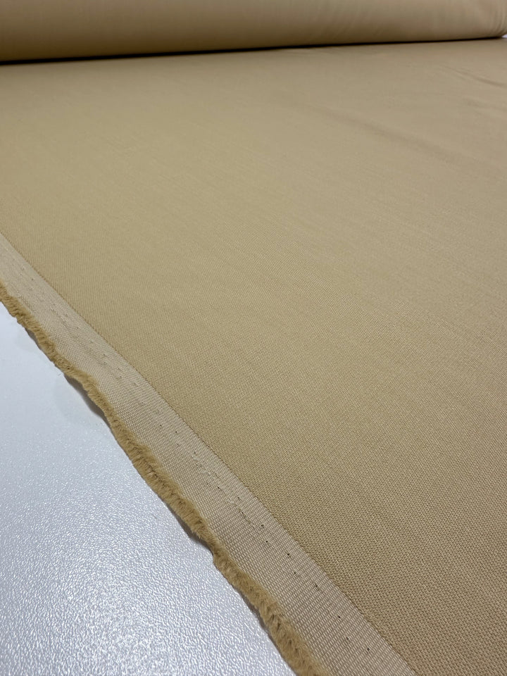 The Stretch Viscose Suiting in Pebble from Super Cheap Fabrics, measuring 130cm wide, is rolled out to highlight its smooth texture and clean edges. The heavyweight fabric rests on a white surface, ready for cutting or further use.