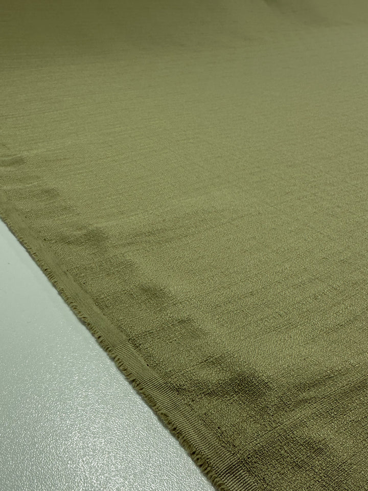 Close-up of Textured Suiting - Cedar by Super Cheap Fabrics, a light green fabric measuring 150cm, laid out smoothly. The textured surface and slightly frayed edges highlight its weave and pattern.