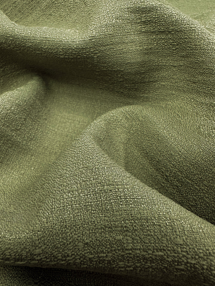 Close-up of Textured Suiting - Cedar - 150cm by Super Cheap Fabrics shows gentle folds and patterns in green twill. Lighting casts shadows, emphasizing the detailed woven surface and soft look, perfect for lightweight formal suiting.