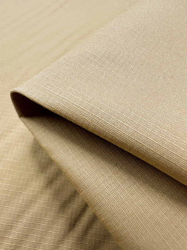 A close-up of the Super Cheap Fabrics "Textured Grid Cotton - Curry - 150cm" shows a neatly folded, light beige cotton with a unique surface pattern, appearing smooth and woven against a matching background.