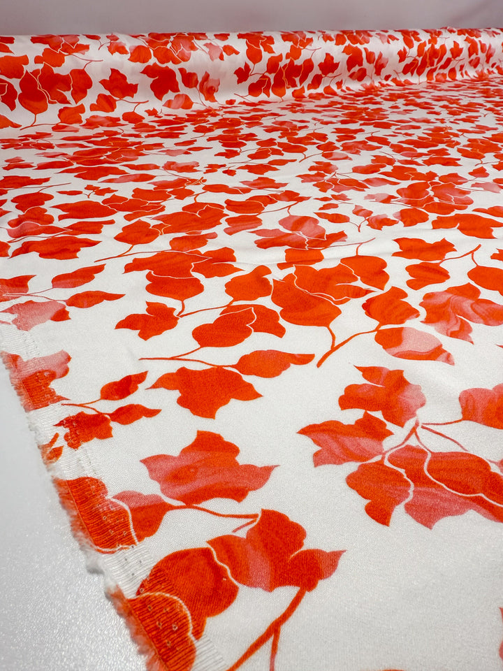 Super Cheap Fabrics' Mercerised Rayon - Flameleaf - 150cm features a smooth, lightweight white fabric with a vibrant red and orange leaf pattern, showcasing its detailed design and lustrous sheen when spread out flat.