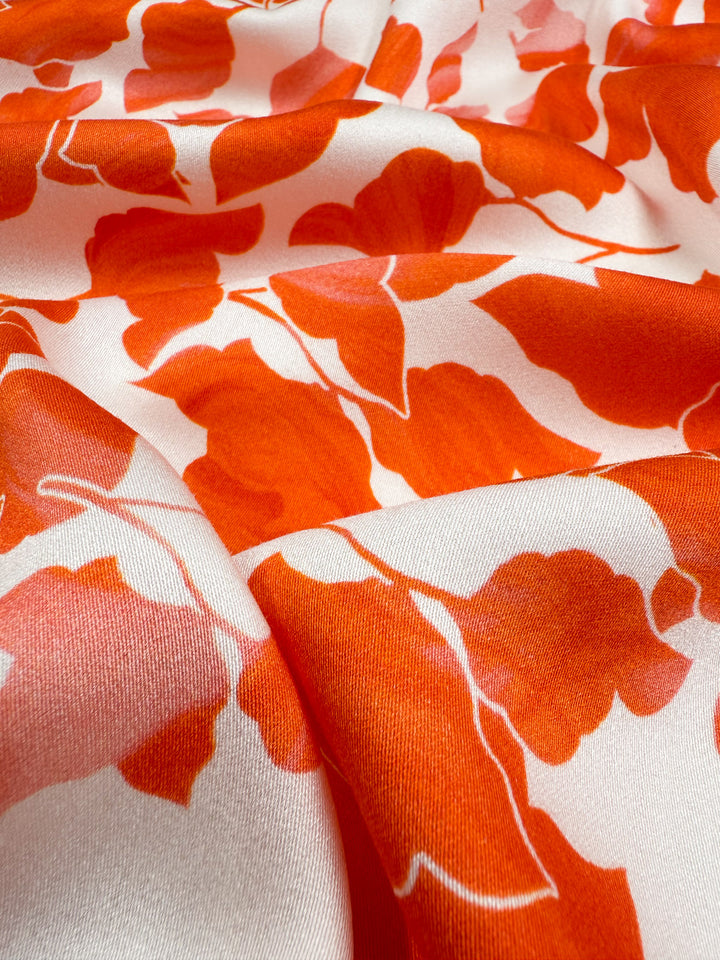 Close-up of Super Cheap Fabrics' Mercerised Rayon - Flameleaf (150cm), featuring a bold, bright orange floral pattern. This lightweight, breathable fabric is gently draped to showcase soft folds and the vivid design.