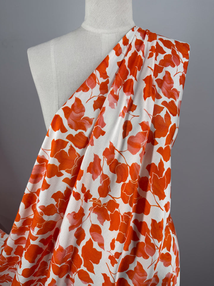 A white mannequin displays Super Cheap Fabrics' Mercerised Rayon - Flameleaf (150cm), featuring a bold orange and red floral design, set against a neutral background.