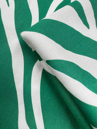 Close-up of Super Cheap Fabrics’ Mercerised Rayon - Tropic Cutout (150cm), featuring green and white breathable rayon with abstract, wavy zebra-like stripes and a folded texture that highlights its color contrast.