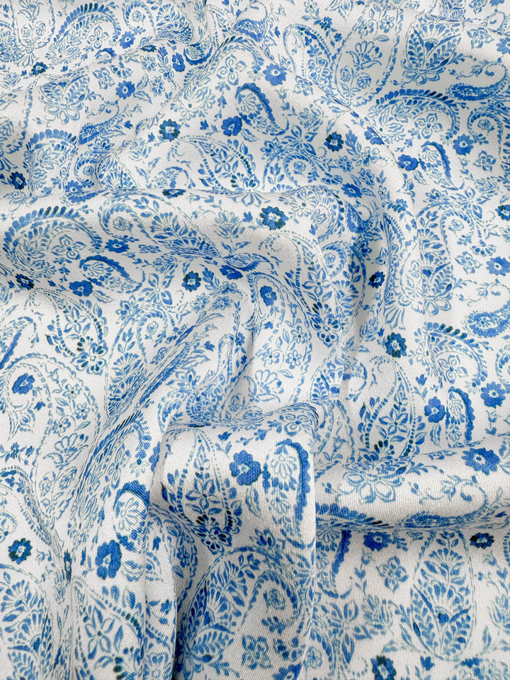 Super Cheap Fabrics' Mercerised Rayon - Delft Vine - 150cm features a silky soft white rayon with detailed blue floral and paisley patterns, showcasing flowing folds and an elegant texture throughout the fabric.