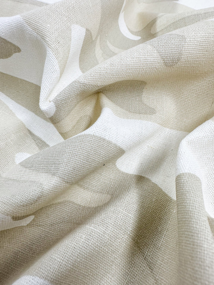 A close-up of the Super Cheap Fabrics Linen Blend - Calm Camo - 137cm reveals its crumpled texture, featuring a subtle beige and white abstract pattern. This cotton blend's coarse feel enhances the play of light and shadows, creating gentle folds for home decor.