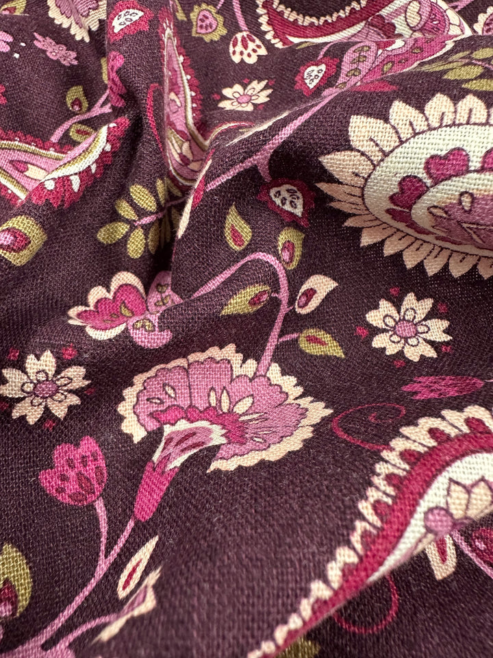 A close-up of the medium-weight Linen Blend - Paisley - 140cm by Super Cheap Fabrics showcases an intricate floral pattern in pink, green, and cream on a dark background. The design features flowers, leaves, and swirling vines for a textured and vibrant look.