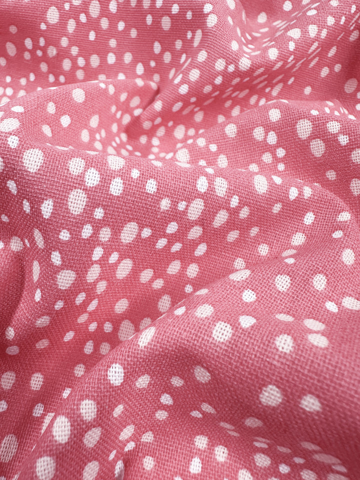 Close-up of Super Cheap Fabrics' Linen Blend - Spotty in mauveglow pink, featuring a pattern of white polka dots. The soft, slightly wrinkled material has varying dot sizes, adding a playful texture perfect for chic home decor accents. Width: 140cm.