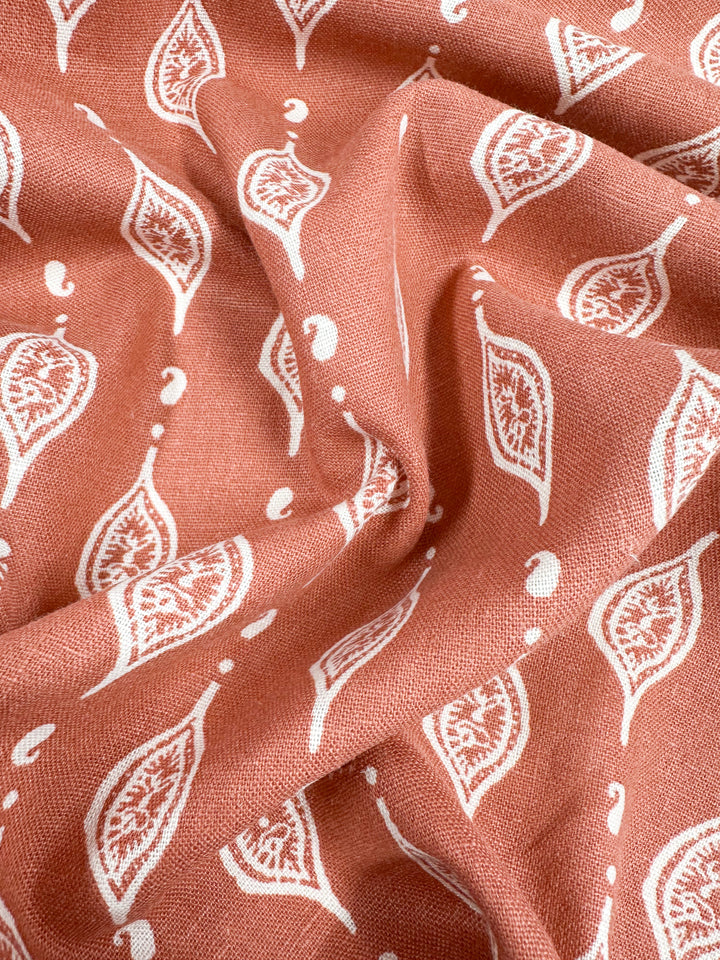 A close-up of Super Cheap Fabrics' "Linen Blend - Repeater - 130cm" in pink, featuring a white paisley pattern perfect for children's clothing. The softly gathered fabric highlights its intricate design and texture, adding a hint of apricot brandy elegance.