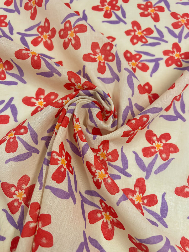 A close-up of Super Cheap Fabrics' Linen Voile - Bloom, revealing a pattern of red flowers and purple leaves against a light beige backdrop. This 150cm cotton linen fabric is artistically gathered in the center, creating a swirling design that accentuates its natural beauty.