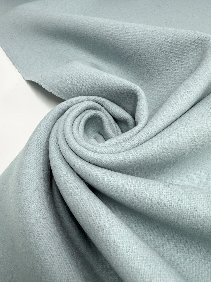 Super Cheap Fabrics' Wool Cashmere - Blue Glass (150cm) is displayed loosely rolled on a flat surface, revealing gentle folds and a subtly textured look that suggests its luxurious softness.